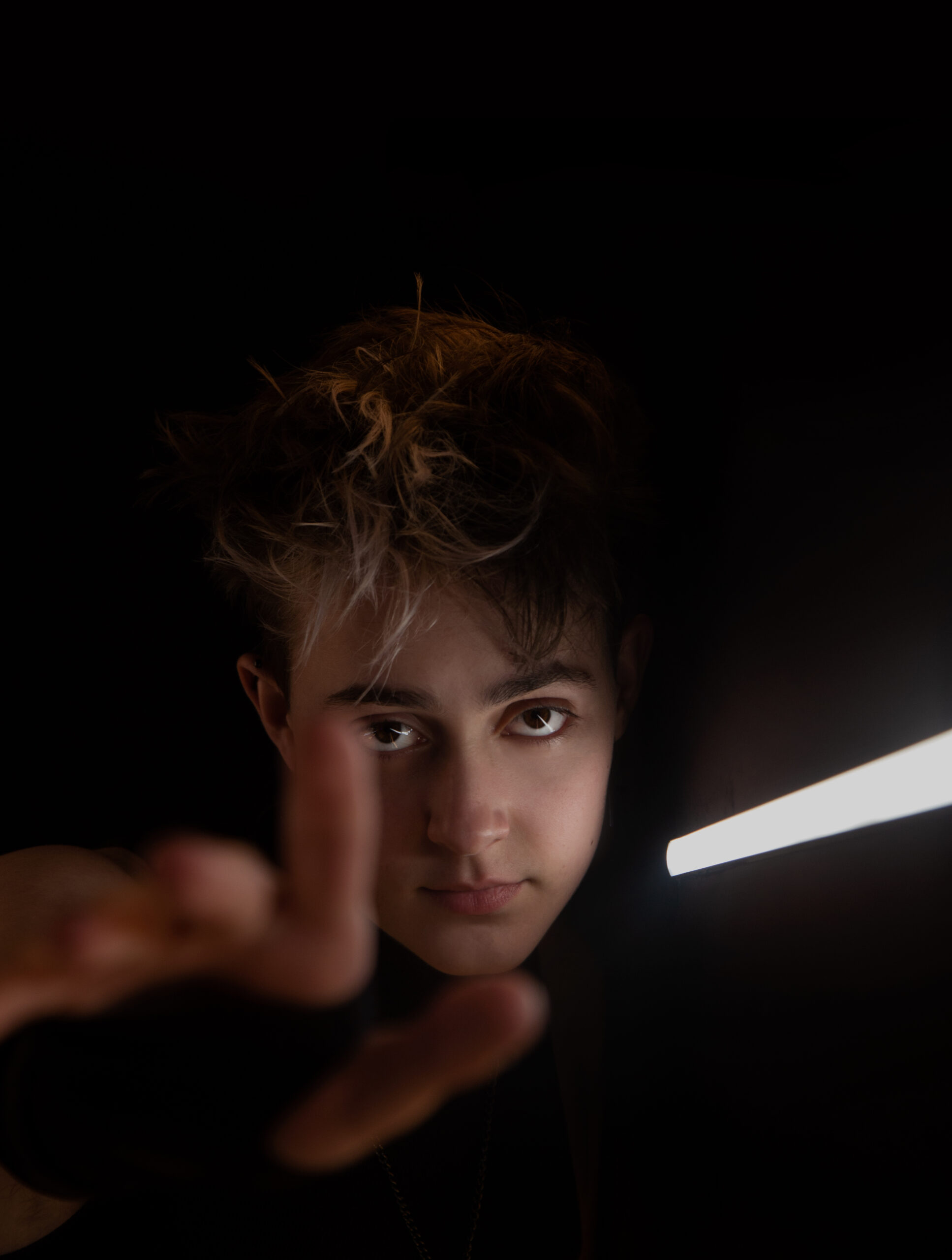 Portrait photography of a man appearing from the dark and holding out a hand illuminated by a single light source